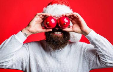 Noel Baba şapkalı sakallı adam. Noel ağacı için iki oyuncağı var. Gözleri kapalı. Noel havası. İyi tatiller. Dekoratif Noel topları olan Noel Baba gözlerinin yanında. Noel süslemeleri ve süsleri