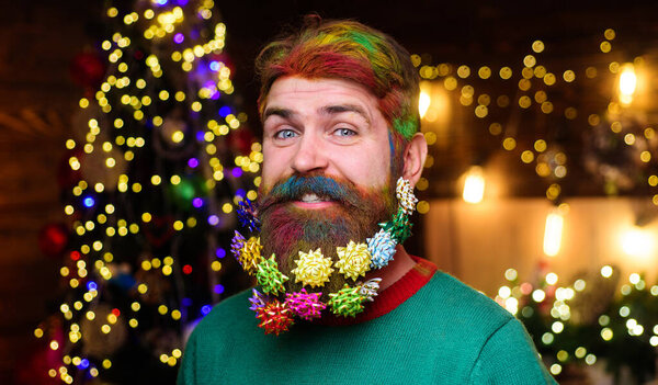 Christmas barbershop advertising. Smiling bearded man with colorful hair and beard with Christmas decorations in beard. Bearded hipster with decorated beard ready for New year party. Closeup portrait