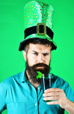 Saint Patricks day celebration. Bearded man in leprechaun hat with glass of green beer. Patrick day pub party. Closeup portrait serious man in green top hat drinking beer. Glass of beer with shamrock