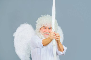 Sevgililer Günün kutlu olsun. Yay ve okla melek kanatlı bir aşk tanrısı. Aşk Tanrısı. Sevgililer Günü meleği aşkın oklarını atıyor. Beyaz peruklu ve oklu melek kostümlü gülümseyen sakallı adam.