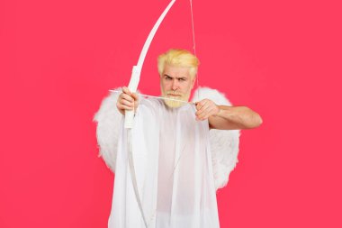 Sevgililer Günü kutlaması. Melek kanatlı bir erkek, hedefe okla ateş eder. Aşk Tanrısı. Sevgililer günü meleği aşkın oklarını atıyor. Ok ve yayla melek kostümü giymiş ciddi sakallı adam.