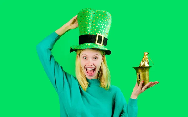 Happy woman in green top hat with small bag of gold. Patricks day celebration. Pot of money for Patricks day party. Blonde girl in green sweater holds leprechaun hat. Traditions of Saint Patrick day