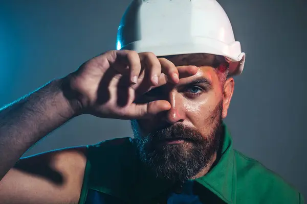 Closeup portrait of tired builder in construction helmet. Fatigued worker wipes sweat from forehead. Hard work at construction site. Heavy profession. Handsome male architect or engineer in hard hat
