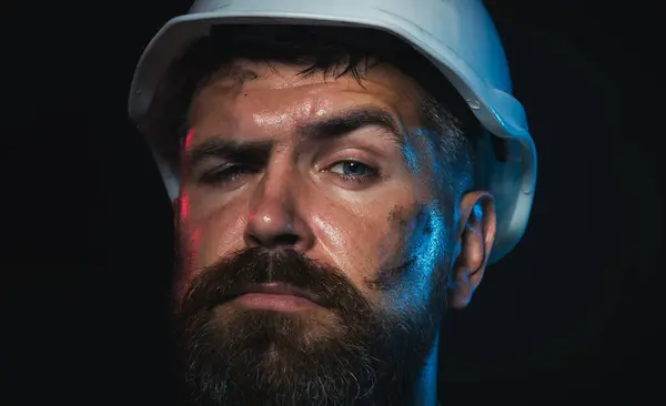 Closeup portrait of construction worker in hard hat. Serious male builder, architect or engineer in protective hardhat. Hard work. Bearded miner or industrial worker with dirty face in safety helmet