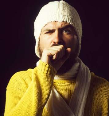 Grip ya da zatürree olmuş bir adam yumruğuna öksürüyor. Hastalıkta grip, soğuk algınlığı ya da bronşit belirtileri var. Süveter giymiş hasta bir adam ve boğazı ağrıyan beyaz bir eşarba sarılı bir şapka. Yakın çekim.