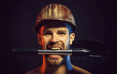 Seksi profesyonel müteahhit, mühendis ya da kürekli koruyucu kasklı tamirci. Yakın plan portre, dişlerinde kürekle sert şapkalı kızgın sakallı adam. İnşaat işçisi, kasketli ve kürekli.