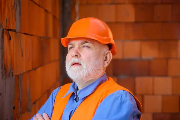 Portrait of construction worker in safety vest and hard hat at work. Bearded architect builder in protective helmet. Professional foreman, craftsman on construction site. Building and home renovation