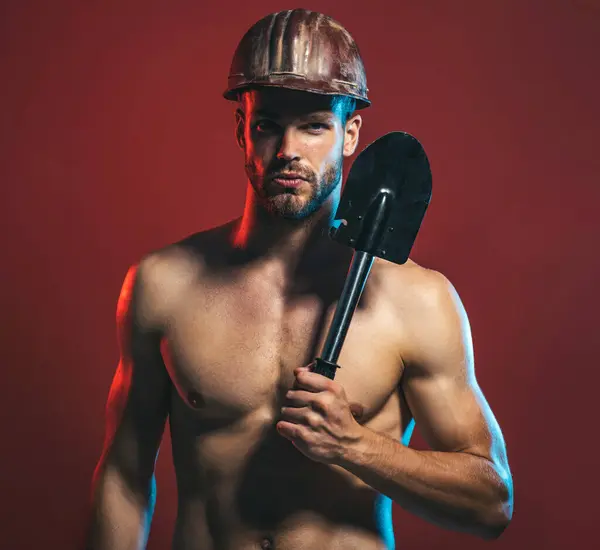 Sexy professional builder in protective helmet with spade. Male architect, repairman in hard hat with strong body. Brutal muscular worker with shovel. Heavy industry, construction and mining concept