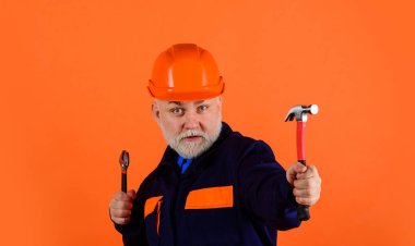 Ayarlanabilir İngiliz anahtarı ve çekiçle inşaat işçisi ya da inşaat işçisi. Ayarlanabilir anahtarı ve çekici olan üniformalı sakallı bir adam. Tamirci, tamirci, tamirci.