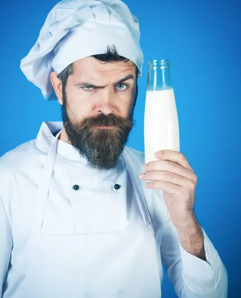 Dairy farmer products. Professional male chef in white apron with glass bottle of milk. Serious bearded cook in chef hat and uniform with bottle of kefir, yogurt or milkshake. Organic healthy food