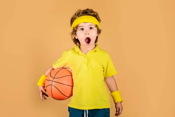 Surprised child boy in sports uniform with basketball ball. Little basketball player in sportswear with ball. Adorable child playing basketball. Sport for children. Healthy lifestyle and training
