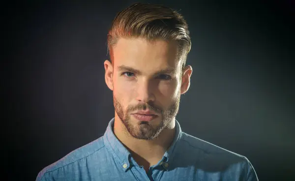 Closeup portrait of serious fashionable bearded man with modern haircut. Handsome unshaven businessman in casual clothes. Pensive attractive guy with stylish hairstyle. Sexy male model in denim shirt