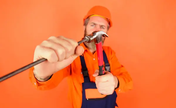Construction worker hammering nails with hammer. Selective focus. Repair service. Hammer and nails. Repairman or carpenter in hard hat hammering nail. Builder, industrial worker with nail and hammer