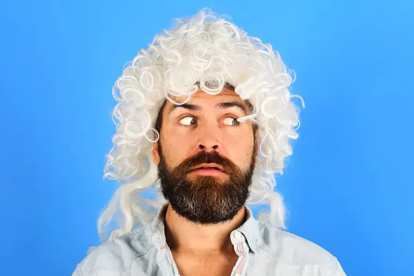 Portrait of surprised man with beard and mustache in white wig. Party time. Stylish bearded male model in curly wig. Fashion concept. Handsome hipster in periwig looking away. Barbershop advertising