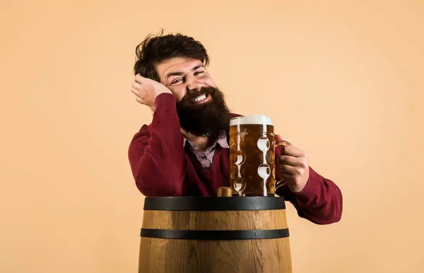 Beer time. Smiling bearded man with mug of beer on wooden barrel. Oktoberfest festival. Stylish handsome guy drinking craft beer at restaurant. Man tasting draft beer at pub or bar. Alcohol drink