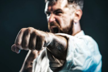 Karate dövüşçüsü jimnastik salonunda yumruk çalışıyor. Yumruğa odaklan. Güç ve motivasyon. Kimonolu çığlık atan adam karate eğitimine hazır. Kızgın karateci dövüş pozisyonunda. Karışık dövüş sanatı