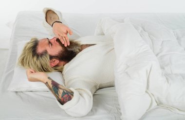 Bornozlu sakallı adam yumuşak beyaz yastığa uzanıp esniyor. Yakışıklı adam evdeki rahat yatakta esniyor ve esniyor. Yataktaki uykucu adam elleriyle ağzını kapatarak esniyor. Günaydın.