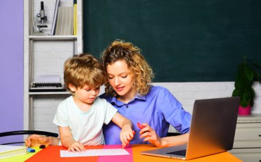 Öğretmen sınıftaki çocuğa çizim, yazma ya da çalışma konusunda yardım ediyor. Eğitimsel süreç. Anne küçük oğluna okuma yazma öğretiyor. Mutlu aile matematiği dersleri. İlkokuldan bir çocuk