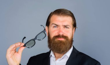 Ciddi sakallı bir adamın portresi güneş gözlüğünü çıkarır. Takım elbiseli yakışıklı adam gözlüklerini çıkarıyor. Resmi giyimli, gözlüklü şık bir iş adamı. Erkek modası. Gözlüklü şık bir iş adamı.