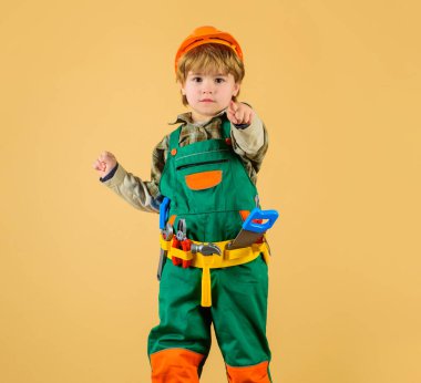 Turuncu şapkalı yakışıklı çocuk, müteahhit üniforması ve alet kemeri seni işaret ediyor. Küçük çocuk inşaatçılık, marangozculuk ya da tamircilik oynuyor. Emniyet kasklı ve takım elbiseli sevimli bir çocuk.