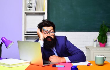Sıkı çalışma. Sınıfta dizüstü bilgisayarla çalışan yorgun erkek öğretmen ya da öğrenci. Okul işi. İş adamı, profesyonel internet öğretmeni ya da masa başında çalışan ya da bilgisayar üzerinde e-öğrenen bir ofis çalışanı