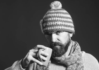 Süveter ve şapkaya sarılı kahve ya da çay eşarplı ciddi bir stil erkeği. Sonbahar ya da kış. Modaya uygun giysiler içinde sakallı adam portresi bardaktan içecek içiyor. Siyah ve beyaz