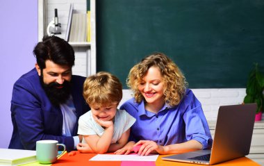 Okuldaki ilk günüm. Özel ders. Küçük çocuk sınıfta ders çalışıyor. Öğretmen erkek ve kadın ilkokuldan çocuğun okul ödevlerine yardım ediyorlar. Annesi ve babası ödev yapan tatlı bir çocuk.