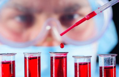 Kan testi. Doktor laboratuvarda hastanın kan örneğiyle çalışıyor. Antikorların tespiti. Serolojik test. Mikrobiyolog, maskeli ve gözlüklü tıp bilimcisi test tüplerindeki kan örneklerini analiz ediyor.