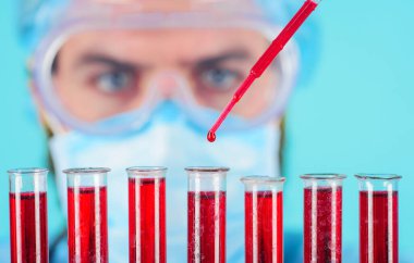 Kan testi. Doktor laboratuvarda hastanın kan örneğiyle çalışıyor. Antikorların tespiti. Hastanedeki serolojik testler. Maskeli ve gözlüklü bir tıp bilimcisi test tüplerindeki kan örneklerini analiz ediyor.