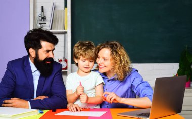 İlkokuldan küçük bir çocuk öğretmen erkek ve kadınla okul ödevi yapıyor. Özel ders. Ebeveynler ve oğulları birlikte okuyorlar. İlkokuldan tatlı bir çocuk, anne ve babasıyla ödev yapıyor.