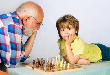 Satranç yarışması. Çocuk büyükbabayla satranç oynuyor. Beyin gelişimi ve mantık kavramı. Küçük çocuk satranç oyununda bir sonraki hamleyi düşünüyor. Masa oyunları. Büyükbaba ve torun satranç oynuyor.