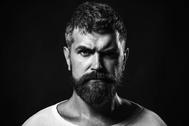 Ciddi sakallı, şık saç stili bir adamın yakın plan portresi. Sıradan tişörtlü, sakallı ve bıyıklı yakışıklı bir adam. Erkekler için moda. Seksi erkek model. Berber modası ve güzellik. Siyah ve beyaz