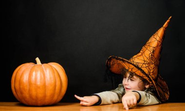 Mutlu Cadılar Bayramı. Cadı şapkalı gülümseyen çocuk Cadılar Bayramı balkabağını işaret ediyor. Şeker mi şaka mı? Sihirli balkabağı. Cadılar Bayramı hazırlığı. Cadılar Bayramı çocuğu ve balkabağı.