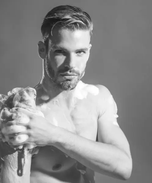 stock image Sexy muscular bearded man taking shower in bathroom. Handsome young man washing body with foamy sponge and moisturizing gel. Morning routine, personal hygiene, body care and skincare. Black and white