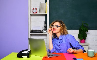 Öğrenme, eğitim ve bilgi konsepti - sınıfta dizüstü bilgisayarla çalışan gülümseyen bayan öğretmen veya üniversite profesörü. Gözlüklü genç kız üniversitede sınav ya da sınava hazırlanıyor.