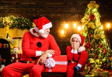 Noel Baba ve küçük Noel Baba çocuk için hediye getirmiş. Noel zamanı. Şaşkın çocuk ve Noel Baba kostümlü gülümseyen sakallı adam Noel için dekore edilmiş odada. Aile tatilleri