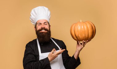 Happy bearded man in chef hat and uniform presenting big pumpkin for restaurant menu. Organic food. Healthy product. Male cook in apron with pumpkin. Autumn recipe. Useful vegetable. Seasonal vitamin clipart