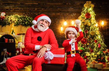 Aile kış tatili. Sevimli çocuk ve Noel Baba kostümü giymiş sakallı, Noel hediyeli, Noel için dekore edilmiş bir oda. Noel Baba ve küçük Noel Baba Noel hediyesiyle evde.