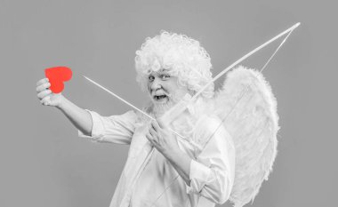 Sevgililer Günü kutlaması. Melek kanatlı ve kıvırcık peruklu mutlu sakallı adam kağıt kalp ve aşkın okunu tutuyor. Ok ve yaylı yakışıklı adam. Kırmızı kalpli sevgililer günü aşığı. Siyah ve beyaz