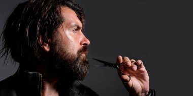 Sakallı yakışıklı adam berber makası tutuyor. Profesyonel berber aletleri. Erkek saç kesimi, moda. Tarz sahibi, saç stili makaslı sakallı adam. Berber dükkanı reklamları için kopyalama alanı. Pankart tasarımı