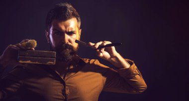 Berber dükkanı servisi. Profesyonel sakal bakımı. Sakallı yakışıklı adam jilet, tahta kutu ve tıraş fırçası tutuyor. Kuaför aletleri ve berber aletleri. Berber dükkanı reklamları için yer kopyala