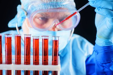 Kan testi. Doktor laboratuvarda kan örneğiyle çalışıyor. Hastanedeki serolojik testler. Tıbbi maske, gözlük ve eldiven giyen bilim adamı veya laboratuvar asistanı test tüplerindeki kan örneklerini analiz ediyor.