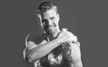 Genç kaslı adam nemlendirici jelle duş alıyor. Erkek kozmetiği. Spa, güzellik, hijyen ve rahatlama. Sabah rutini. Cilt bakımı ve vücut bakımı. Gülümseyen adam vücudu süngerle yıkıyor. Siyah ve beyaz