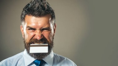 Beyaz gömlekli ve mavi kravatlı bir işadamının dişlerinde manyetik şerit olan bir kredi kartı var. Bankamatik ya da ödeme kartı olan yakışıklı sakallı adam, yakın plan portre. Banka servisi. Reklam için boşluk kopyala