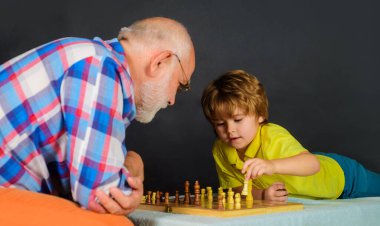 Satranç yarışması. Satranç oyununda sıradaki hamleyi düşünen tatlı çocuk. Dedem çocuklara satranç öğretiyor. Mantığın ve stratejik düşüncenin gelişimi. Büyükbabam ve torunum evde satranç oynuyorlar.