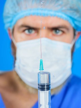 Cerrahi maskeli erkek doktor enjeksiyon için şırınga hazırlıyor. Seçici odaklanma. Doktor şırıngaya ilaç fışkırtıyor. Aşılama. Üniformalı doktor şırıngada aşı taşıyor.