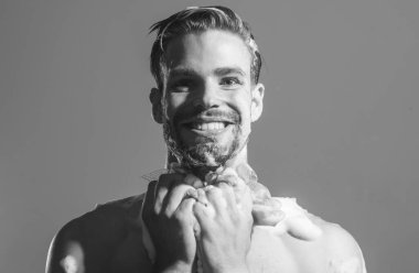 Duş için erkekler kozmetik ürünleri. Duş jeliyle banyoda yıkanan gülümseyen adam. Gündelik hayat. Erkek vücut bakımı ve cilt bakımı. Duşta sabunlu süngerle yıkanan kaslı bir adam. Siyah ve beyaz