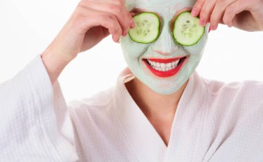 Kil kozmetik maskeli ve gözlerinde salatalık dilimleri olan kadın portresi. Cilt bakımı ve kozmetik prosedürleri. Yüzünde maske ve gözlerinde salatalık olan gülümseyen bir kız. Doğal malzemeler.