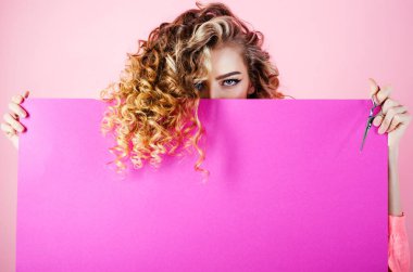 Kıvırcık saçlı güzel kız elinde pembe reklam panosu ve berber makası tutuyor. Parlak makyajlı ve saçı afro saçlı genç bir kadın kuaför makası tutuyor. Saç bakım ürünleri veya kuaför salonu için yer kopyala