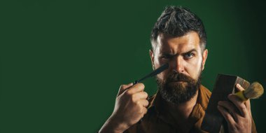 Berber dükkanı aksesuarları. Düz usturalı, tahta kutulu ve tıraş fırçalı bir berber. Sakal bakımı. Tıraş olmak için tıraş bıçağı olan ciddi sakallı bir adam. Berber dükkanı reklamı. Bayrak tasarımı. Boşluğu kopyala